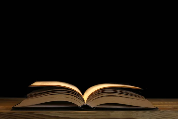 Siyah arkaplandaki ahşap masa gecesi ruh hali üzerine açık bir kitap. Metnin için kopya alanı ile birlikte.