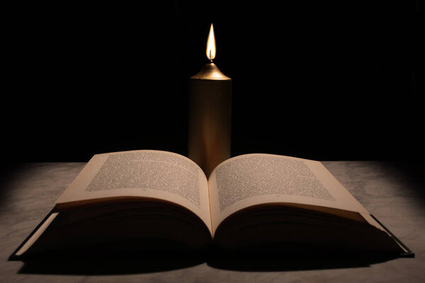 Candle and open book on a marble board on black background and copy space for your text