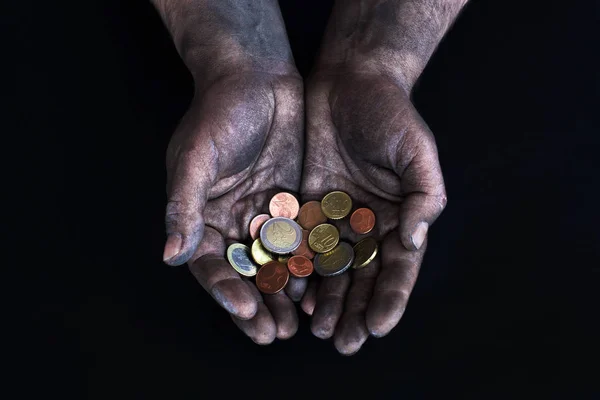 Dirty male hands of a worker holding the euro and euro cents on a dark background. Low-paid work. Money in the hands of a beggar. Low salary.
