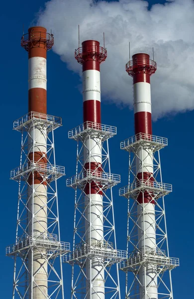 Drie pijpen fabriek met rook op blauwe hemelachtergrond — Stockfoto