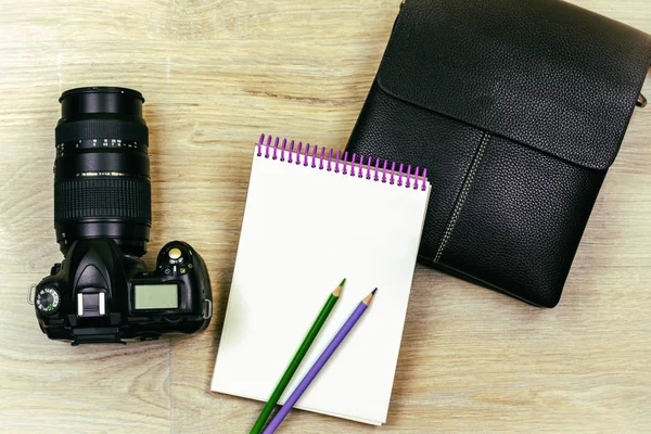 Плоский лежал. SLR камера, блокнот, два карандаша и мужская сумка лежат на текстуре дерева — стоковое фото