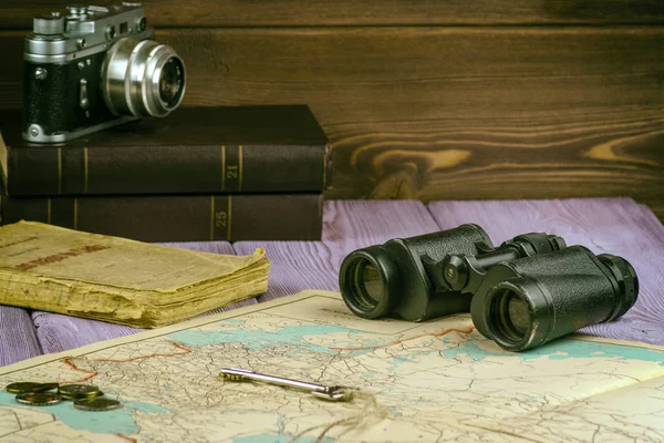 Auf dem Tisch lagen ein altes Buch, eine Landkarte, Münzen, ein Schlüssel und ein Fernglas. Es gibt auch eine Filmkamera. — Stockfoto