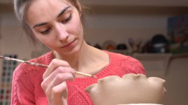 Püskül kullanarak kil pot Kenarları yumuşatma üzerinde yoğunlaşmış bir kız ustası closeup görünümü.