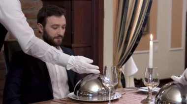 İki garson aynı anda sofra kapak - saygın sakallı adam önünde yemek takım elbiseli gösterilen cloche açılır. İyi yemek restaurant konseptini.