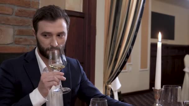 Бородатий чоловік у костюмі пахне склянкою білого вина, а потім накриває і розкручує склянку перед тим, як зробити ковток . — стокове відео