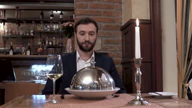 Restoran ziyaretçi kamera önünde oturuyor. Garson sofra kapak - çanak gösterilen cloche açılır. İyi yemek restaurant konseptini.