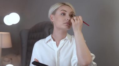 Shorthaired sarışın bir kadın onun göz kapaklarını göz farı koyarak dışarı kamera taşır.