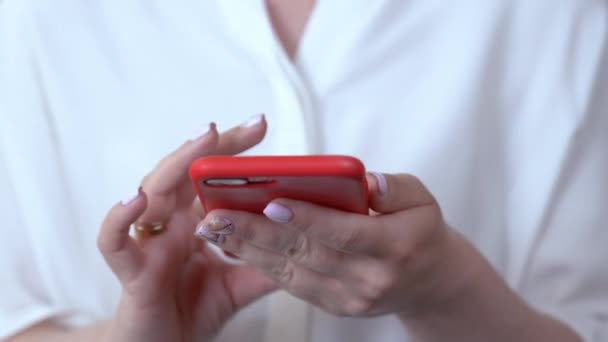 Nahaufnahme von Frauenhänden, die ein Telefon in einer roten Hülle halten, wählt eine Telefonnummer und bringt das Telefon ans Ohr. — Stockvideo