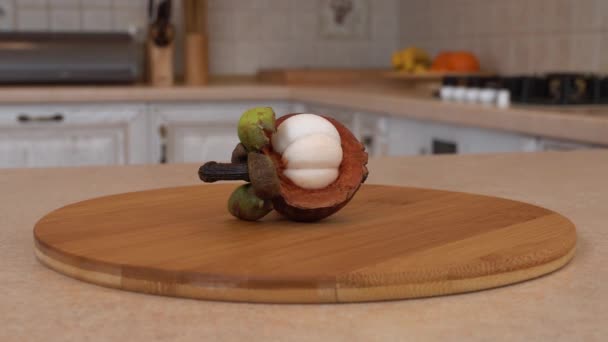 Το ήμισυ του μωβ mangosteen στο πιάτο μπαμπού. Περιστρεφόμενη κάμερα με λευκό κουζίνα στο παρασκήνιο. Dolly-shot. — Αρχείο Βίντεο