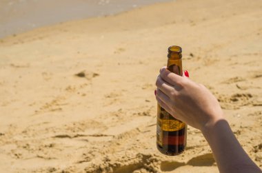Kadın el ile sahilde elinde bira şişesi