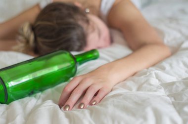 Büyük kavram, alkol. Genç kadın, sarışın, çok fazla alkol içtikten sonra yatakta bayıldı. El, bir şişe şarap şarap.