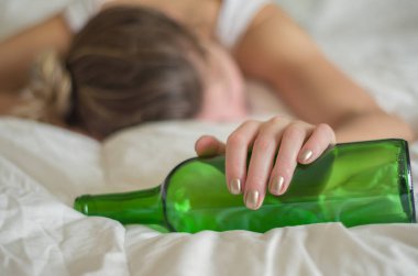 Büyük kavram, alkol. Genç kadın, sarışın, çok fazla alkol içtikten sonra yatakta bayıldı. El, bir şişe şarap şarap.