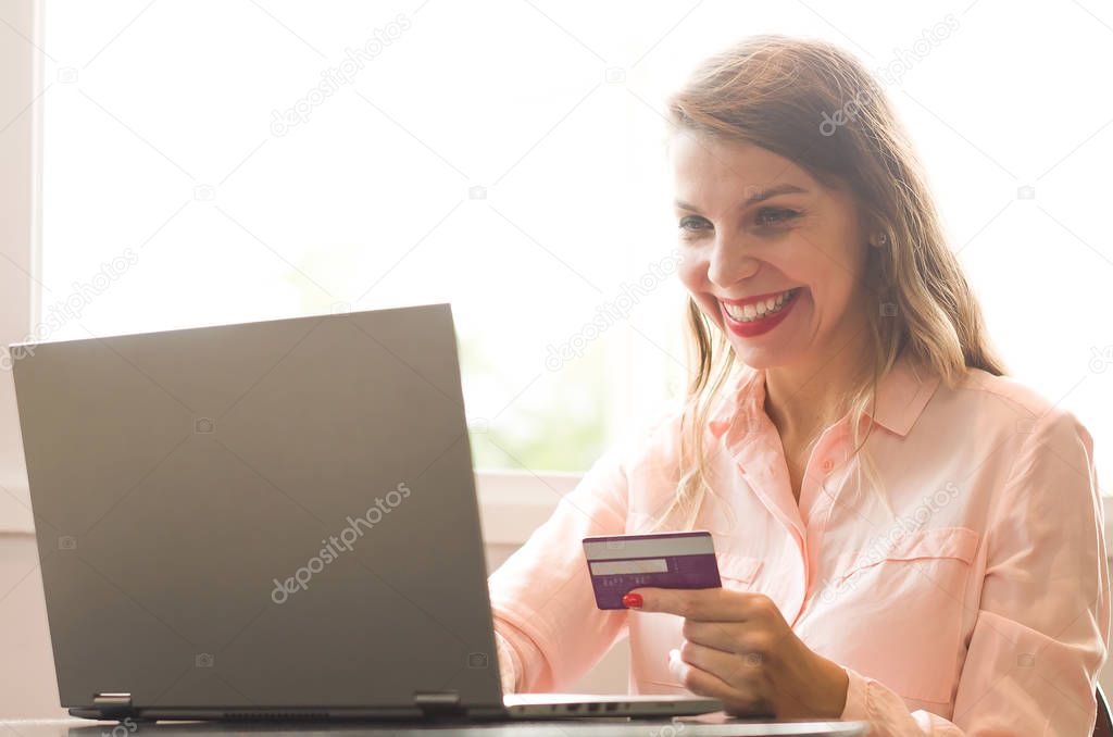 Young blond caucasian woman happy shopping on the internet, credit card in hand.