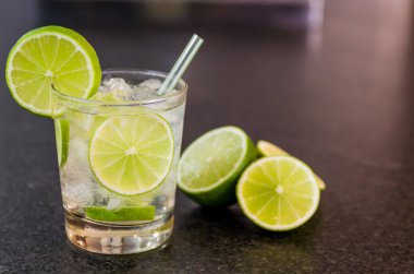 Caipirinha, geleneksel Brezilya alkollü içeceği, şeker, limon, damıtılmış kamış (cachaca) ve buzdan yapılan tipik içecek. İçindekiler ve siyah granit yüzeydeki içecek..