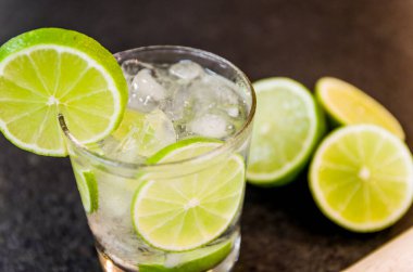 Caipirinha, geleneksel Brezilya alkollü içeceği, şeker, limon, damıtılmış kamış (cachaca) ve buzdan yapılan tipik içecek. İçindekiler ve siyah granit yüzeydeki içecek..