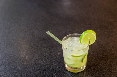 Caipirinha, geleneksel Brezilya alkollü içeceği, şeker, limon, damıtılmış kamış (cachaca) ve buzdan yapılan tipik içecek. İçindekiler ve siyah granit yüzeydeki içecek..