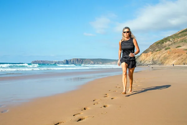 Mulher madura e saudável correndo na praia — Fotografia de Stock