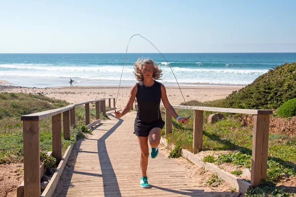 Rijpe vrouw uitoefening springen touw hoge knieën op het strand — Stockfoto