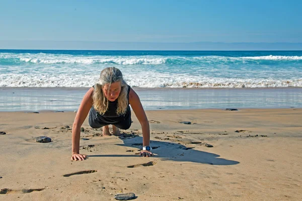 Спортивна зріла жінка робить вправи на пляжі в атласі — стокове фото
