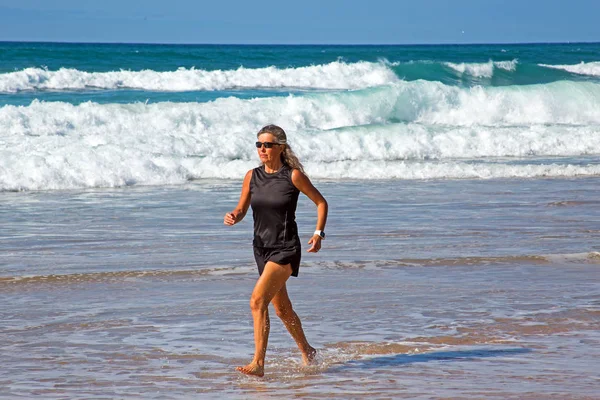 Deportiva mujer madura trotando a lo largo de la playa en el atlántico oc —  Fotos de Stock