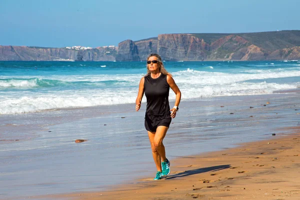 Спортивна зріла жінка біжить уздовж пляжу на атлантичному восьмій — стокове фото