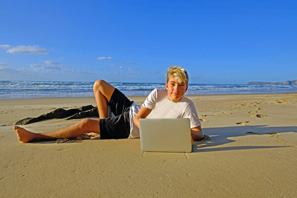 Young guy at the beach working on his laptop