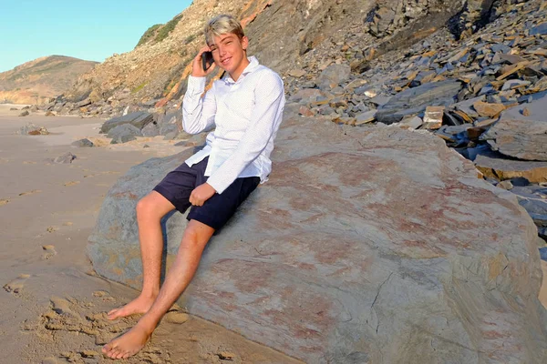 Молодой парень делает звонок на пляже — стоковое фото