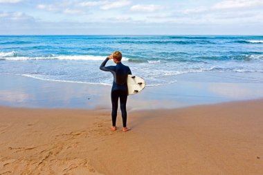 Genç adam sörf yapmadan önce dalgalara bakıyor.