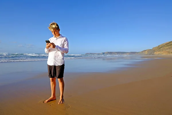 Mladý muž na pláži píše text na svůj mobilní telefon — Stock fotografie