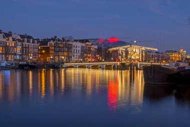 Amsterdam 'dan şehir manzarası Amstel nehrinin kıyısında Hollanda' da gece vakti Minik Köprü ile