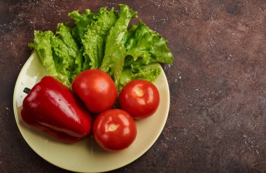 Taze sebzeler, biberli domatesler ve kahverengi arka planda bir tabakta marul.