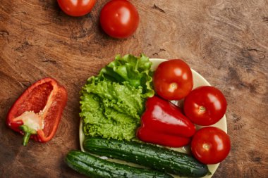 Taze sebzeler, biberli domatesler, salatalıklar ve marul, ahşap bir arka planda, izole edilmiş bir tabakta.