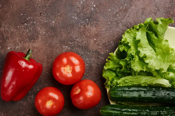 fresh veggies pepper tomatoes cucumbers and lettuce on a plate on a brown background isolated