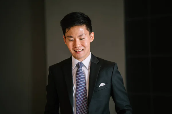 Portrait of a Chinese Asian professional lawyer against a dark background. He is wearing a dark suit, white shirt, blue tie and pocket square. He is relaxed and confident.