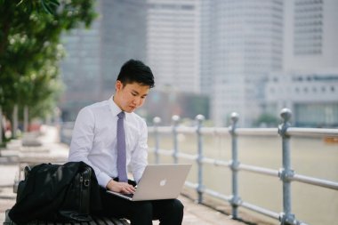 Singapur Nehri boyunca onun dolma kalem ile bir dizüstü dizüstü bilgisayar ile gün içinde yazılı Asya adam portresi. O profesyonel bir beyaz gömlek giymiş, ama onun ceket kravat vardır.