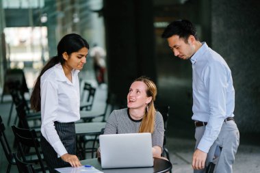 farklı bir takım 3 kişi bir dizüstü bilgisayar etrafında bir tartışma gün açık bir alanda yaşıyorsanız. Gülümse ve konuşmak gibi enerjik ve neşeli vardır.