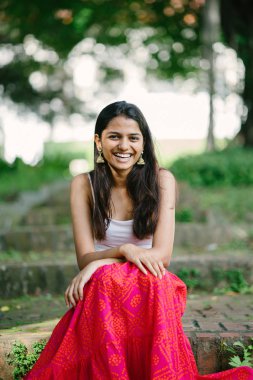 Günde bir parkta oturan çekici, genç Hint (Asya) kadın portresi adımlar.