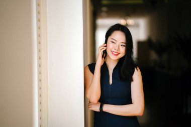 Onun smartphone bir pencere günde kullanan bir genç ve çekici Çinli Asyalı kadın portresi. O bir profesyonel koyu mavi elbise giyiyor ve gülümseyen.