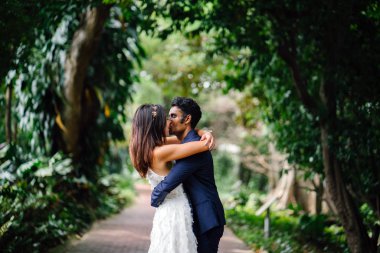 Irklararası çift düğün çekim güzel bir parkta gündüz portresi. Bir yol tutuşun gibi bir Hintli ve Çin nişanlısı tutkuyla öpüşme.