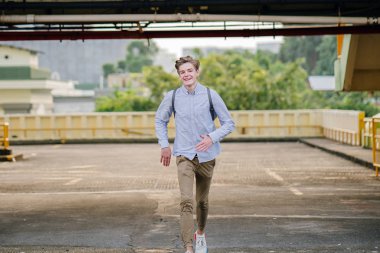 Asya araba parkında gün batımında kameraya Sprint bir genç ve yakışıklı beyaz genç dinamik portresi.