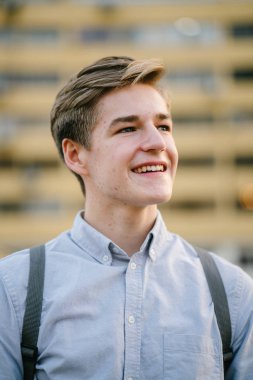 dikey bir genç ve çekici beyaz beyaz adam (turist veya öğrenci) oturma ve gündoğumu veya günbatımı Asya beton bir araba parkta gülüp. O gülümsüyor ve rahat.