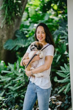 Onun köpeği ve yeşil bir parkta kamera için sıcak bir günde parkta gülümseyen genç bir Pan Asya kadın portresi. Köpek oyuncak doğurmak shih tzuh olduğunu.