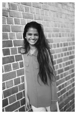 Ayakta infront bir genç ve çekici Hint Asyalı kadın portresi şehirde bir sokakta bir tuğla duvar. Sıcak güneş gülümsüyor.