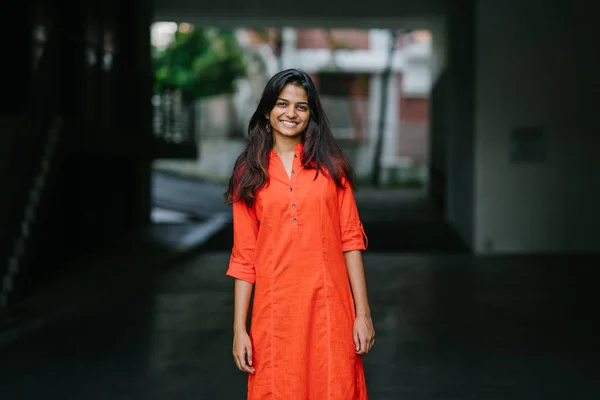 迷人和年轻的印度妇女对城市背景微笑 她穿着一件橘黄色的衣服 — 图库照片