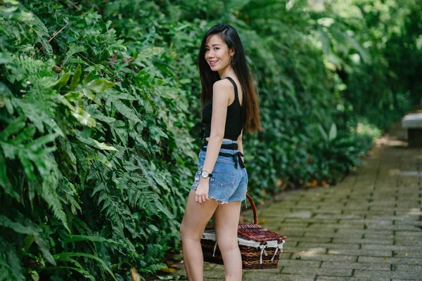 Portrait of a young Asian Chinese woman . She is surrounded by lush, verdant greenery and plants. She is dressed comfortably and stylishly