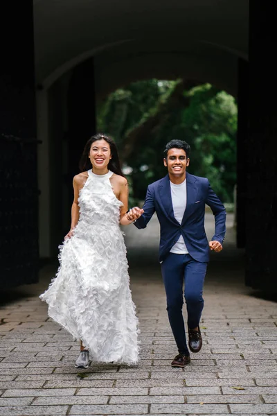 在新加坡的一个公园里 从事异族的亚裔情侣朝摄像机跑去 一个印度男人和他的中国妻子握着手 高兴地笑着跑 — 图库照片