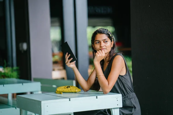 Candid portrait of an attractive and young Indian Asian professional woman reading her tablet or e reader. She is in warm, cosy cafe or coworking space. She is smiling while she reads her tablet.