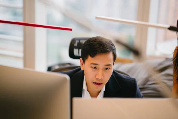 young Chinese Asian trader and banker in finance looks at his screen in intense concentration. He is dressed in a professional suit and in an office.