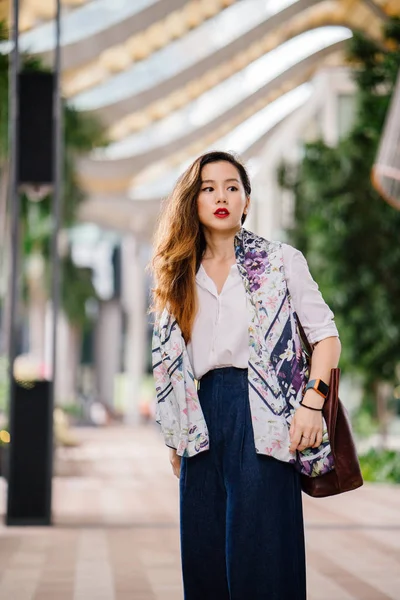 A young and stylish Chinese businesswoman in the city in Singapore. She is Chinese (Singaporean) and is dressed professionally and elegantly. She is relaxed and smiling at the camera.