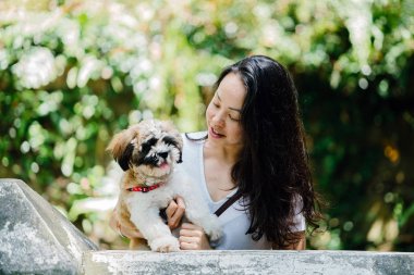 Onun köpeği ve yeşil bir parkta kamera için sıcak bir günde parkta gülümseyen genç bir Pan Asya kadın portresi. Köpek oyuncak doğurmak shih tzuh olduğunu.